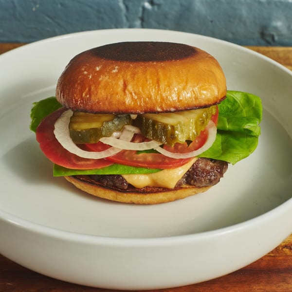 A Blue Road Burger with lettuce, tomato, onion, pickles, and cheese on a white plate.