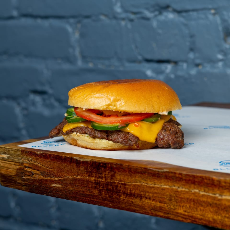 Blue Road Burger with melted cheese, tomato, and jalapeños on a wooden board.