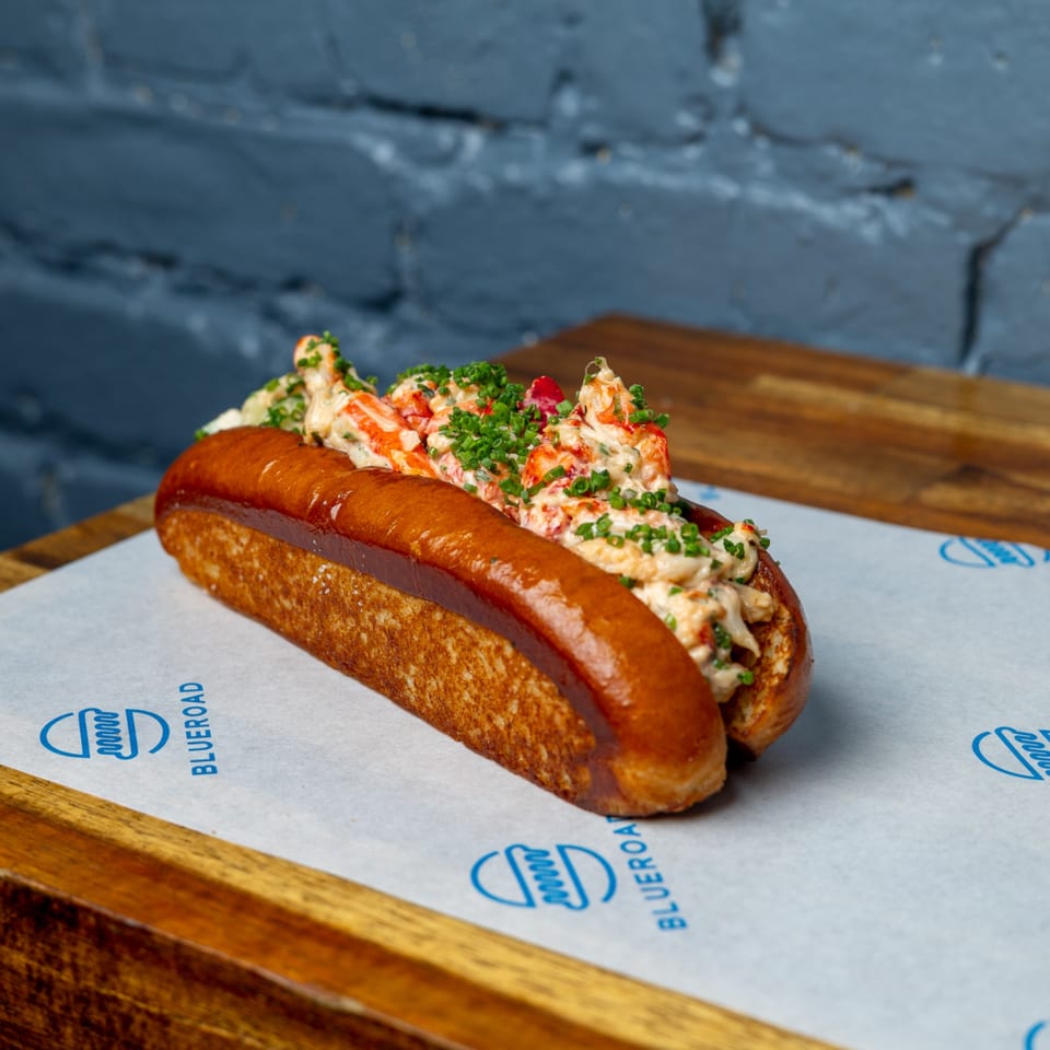 A Blue Road Burger lobster roll, filled with creamy lobster meat and chives, on branded paper.