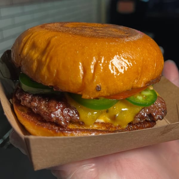 A Blue Road Burger with melted cheese, jalapeños, and a shiny bun in a cardboard tray.