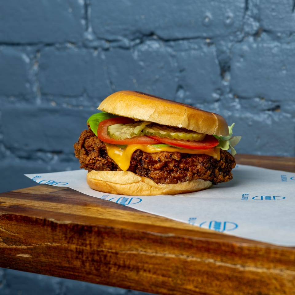 Blue Road Burger's crispy fried chicken sandwich with melted cheese, lettuce, tomato, and pickles.