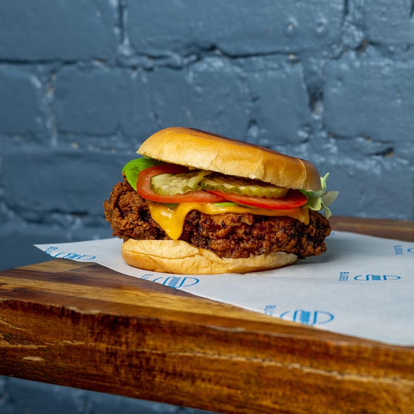 Blue Road Burger's crispy fried chicken sandwich with melted cheese, lettuce, tomato, and pickles.
