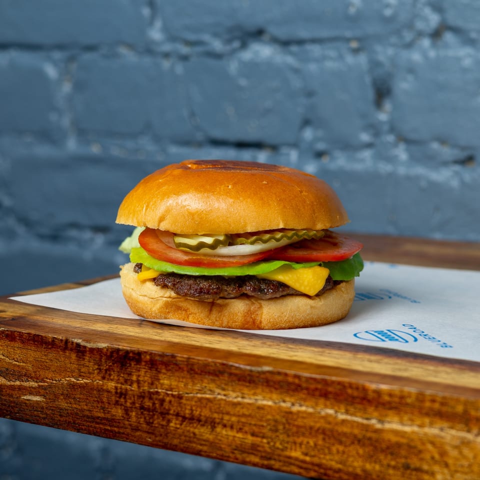 Blue Road Burger with cheese, lettuce, tomato, onion, and pickles on a wooden board.