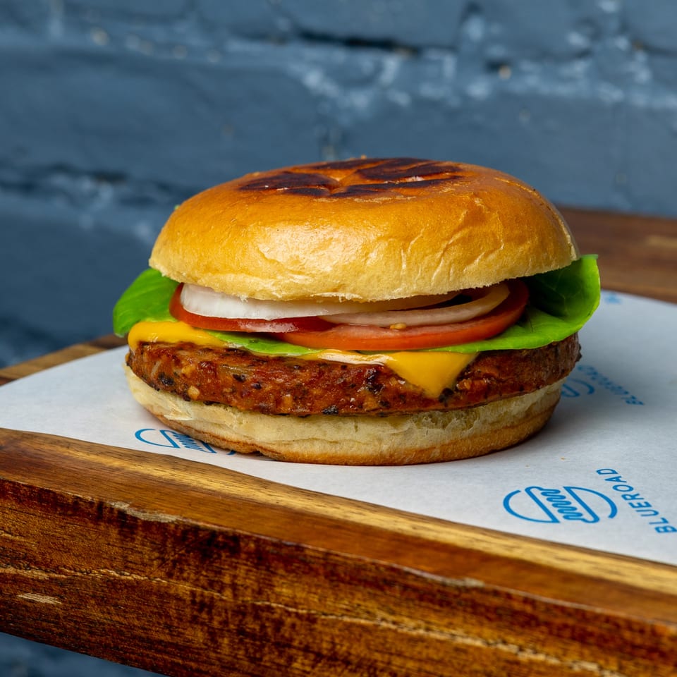 Blue Road Burger with a patty, melted cheese, lettuce, tomato, and onion on a wooden board.