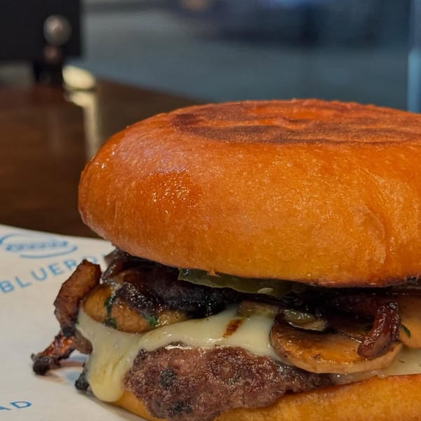 Close-up of a Blue Road Burger with melted cheese, mushrooms, and caramelized onions on a brioche bun.